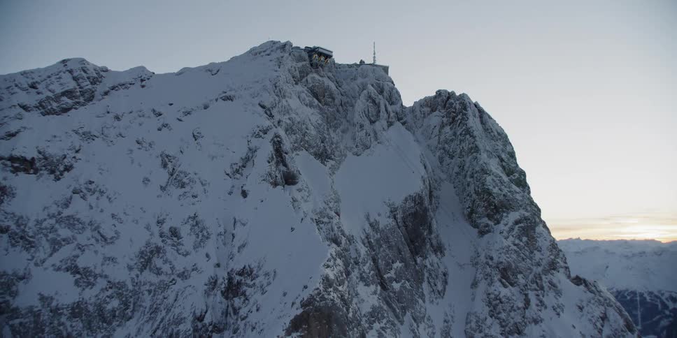The mountain is covered with snow and ice with a building at the top