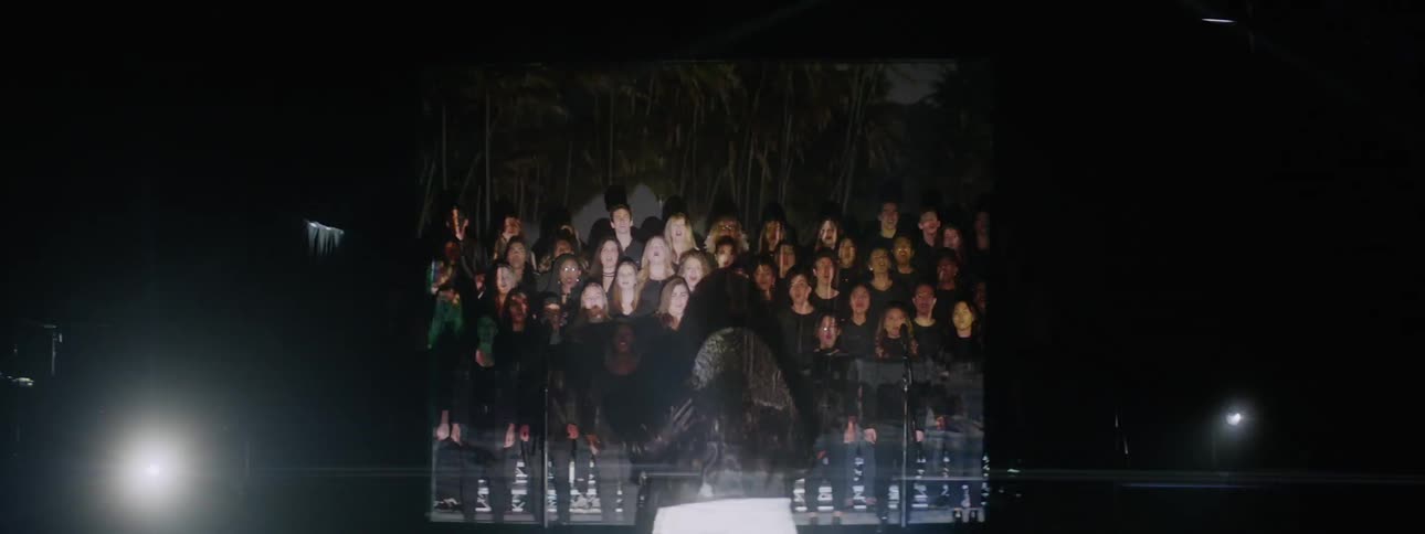 Lights and projected images flash around a choir as it sings on a stage