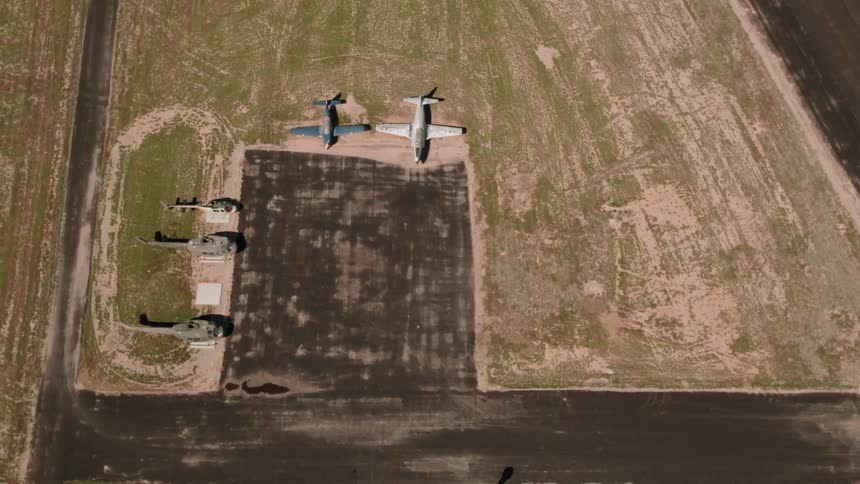 Airplanes and helicopters are sitting idle at a rural airfield in daylight