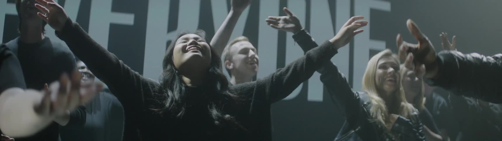 Several people smile and wave their arms as lights flash behind them