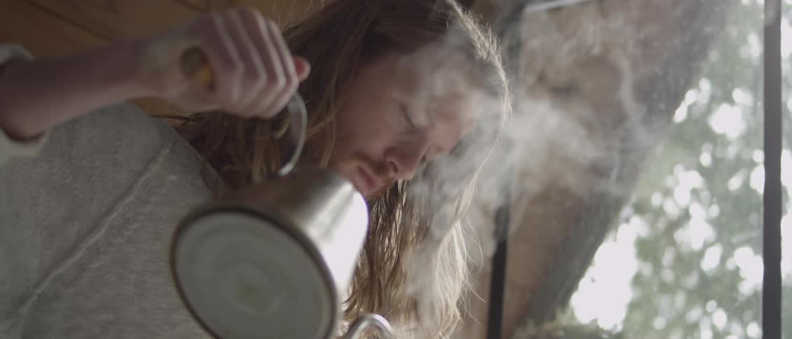 A man is pouring hot water from a kettle inside a tent in daylight