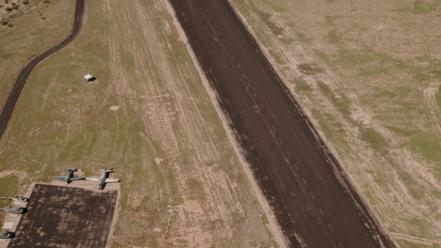 Helicopters and planes are parked to the side of a dirt runway