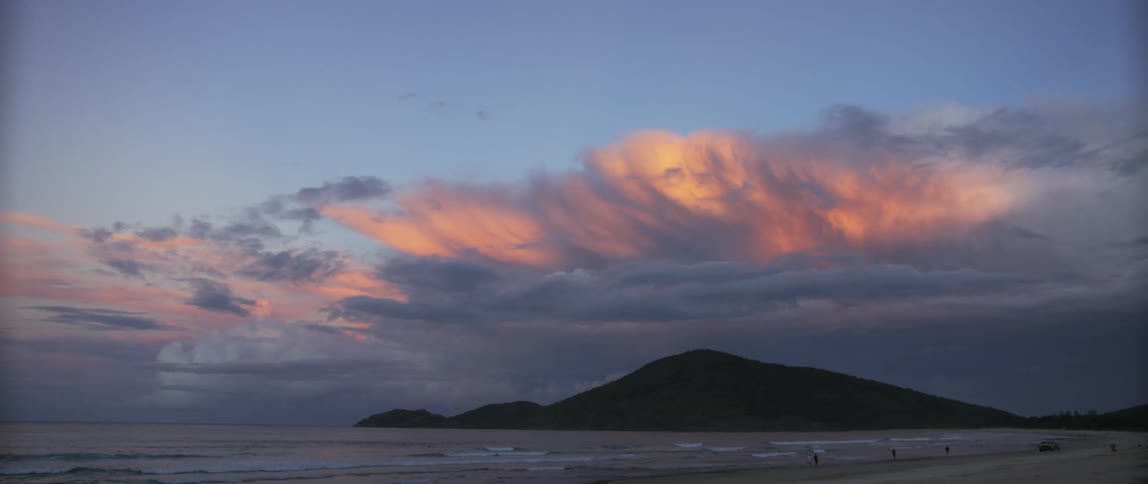 View of a shore with some hills in the distance at sunset