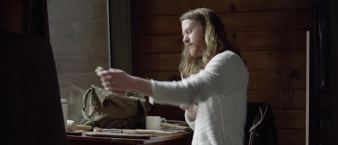 A man is sitting at the table carving some wood