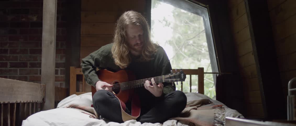 Man sitting on bed is playing the guitar