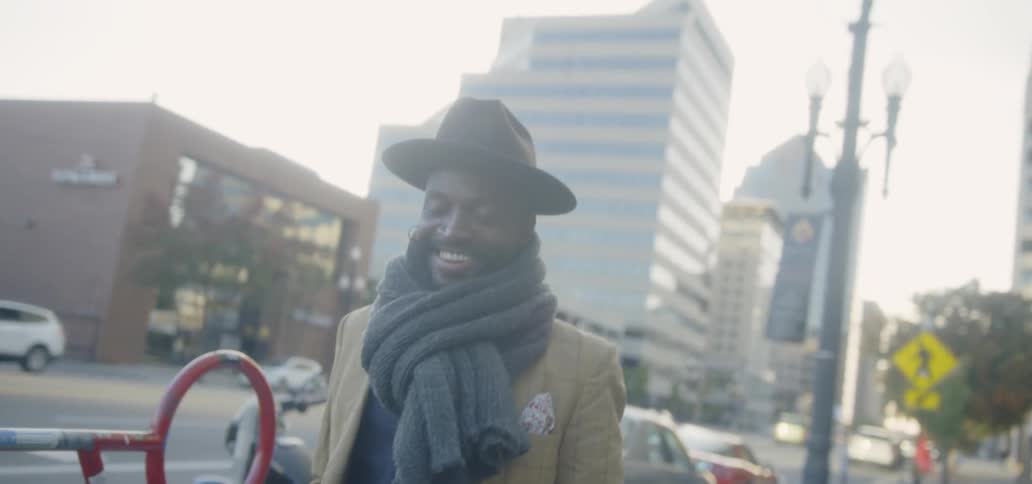 A man smiles while walking on a city sidewalk
