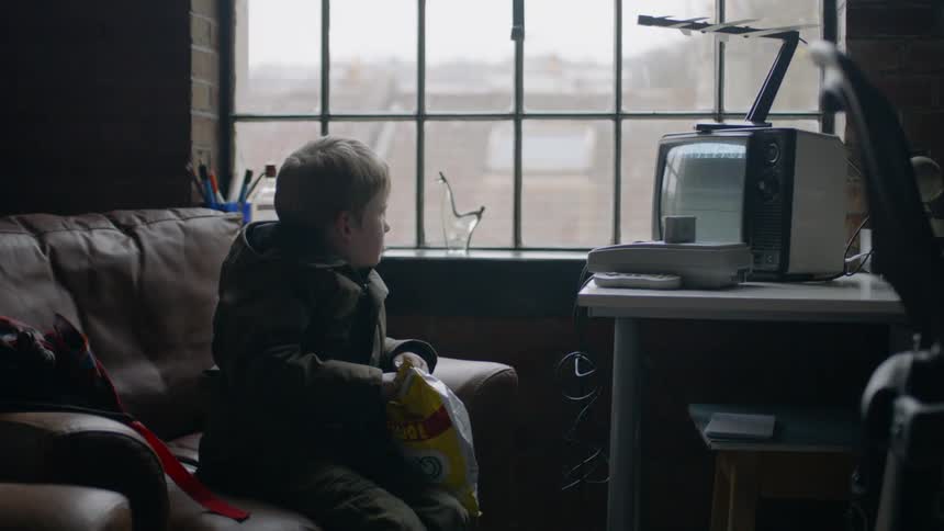 A boy sits on a couch with chips watching a tv playing static