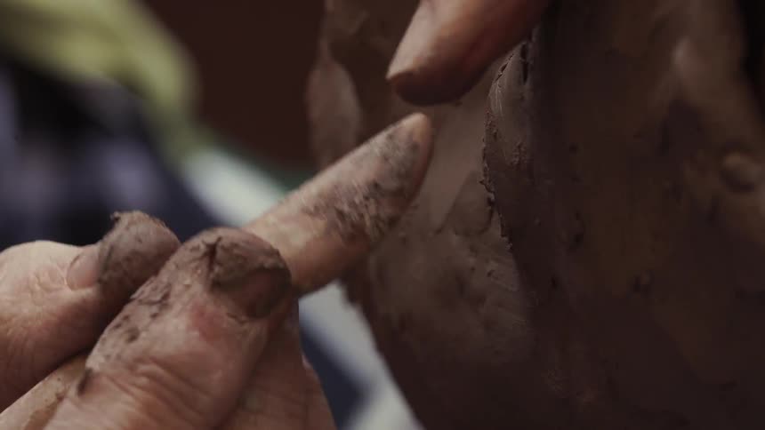 A sculptor models clay with a tool