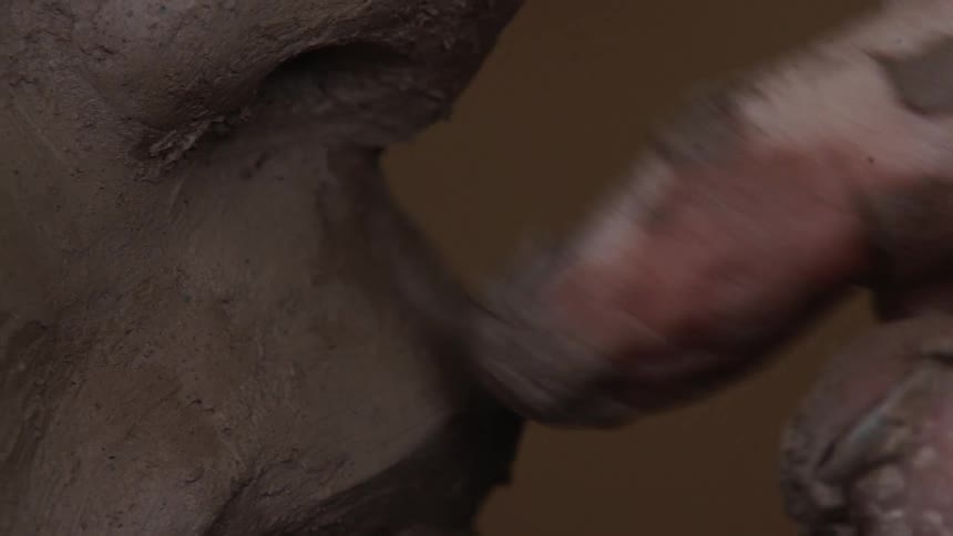 A sculptor models clay with their hand