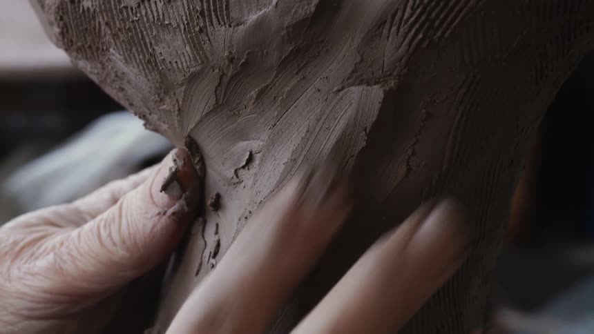 A person forms a clay sculpture