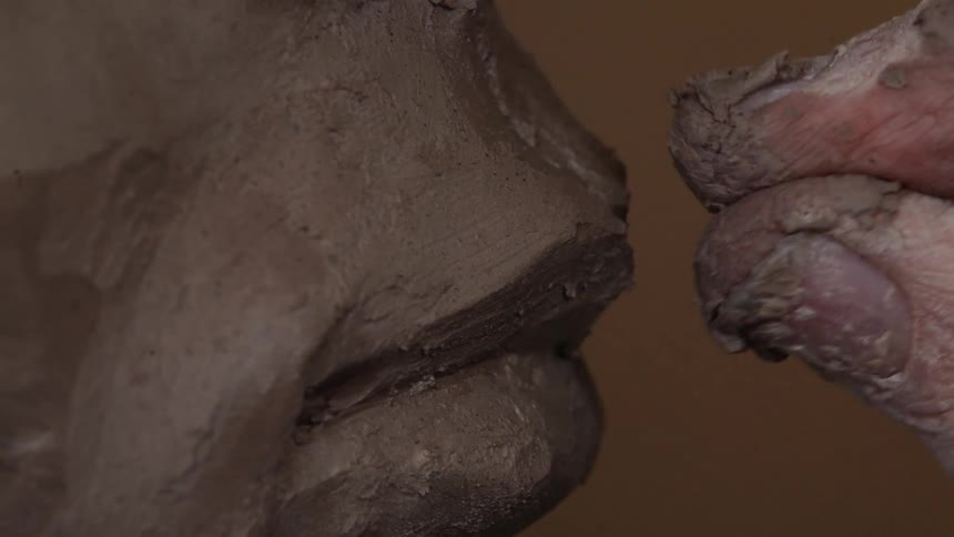 A sculptor shapes the mouth on a clay piece