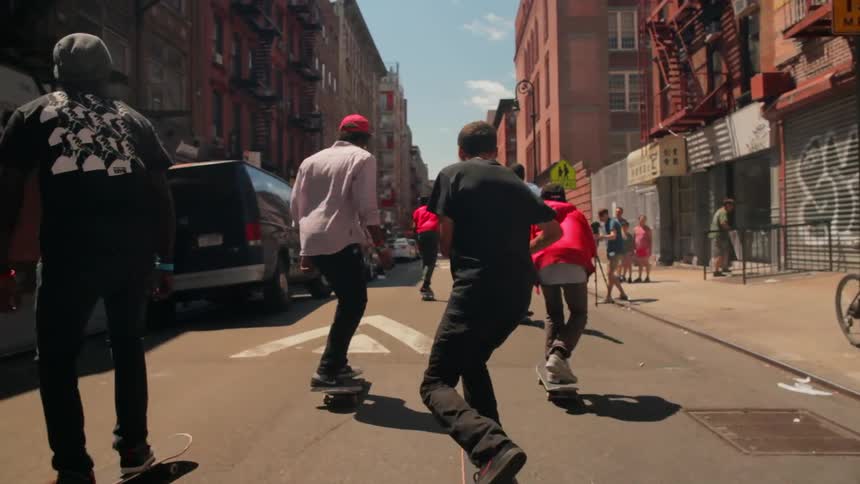 A group of teenage boys are riding skateboards down a city street in daylight
