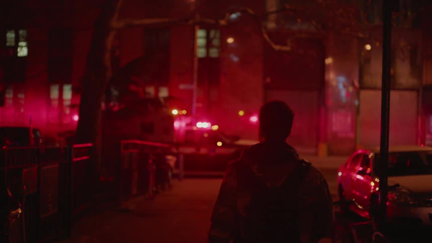 Man walks down a dark street aglow with emergency lights