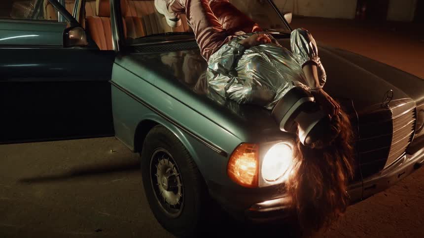 A woman lays on the green car using a virtual reality headset