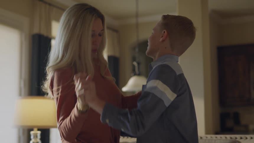 A mother and son dance in a living room