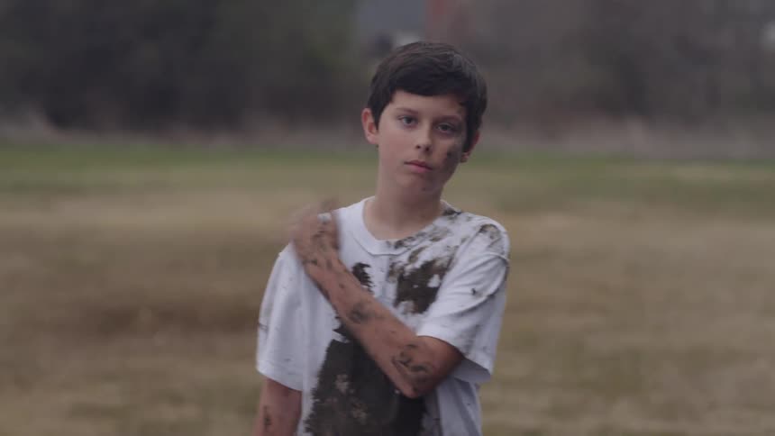 A muddy boy brushes his shoulders