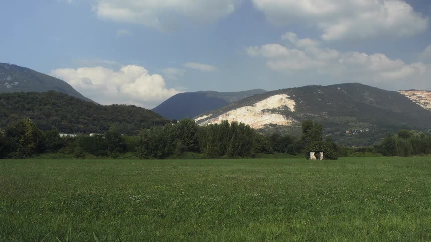 Clouds float above mountains and a grassy field