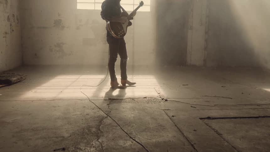 A guitarist stands inside an empty room