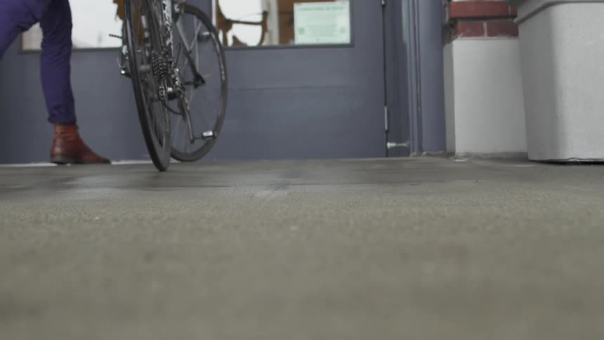 A person is getting off their bicycle and pushing it as they enter a building