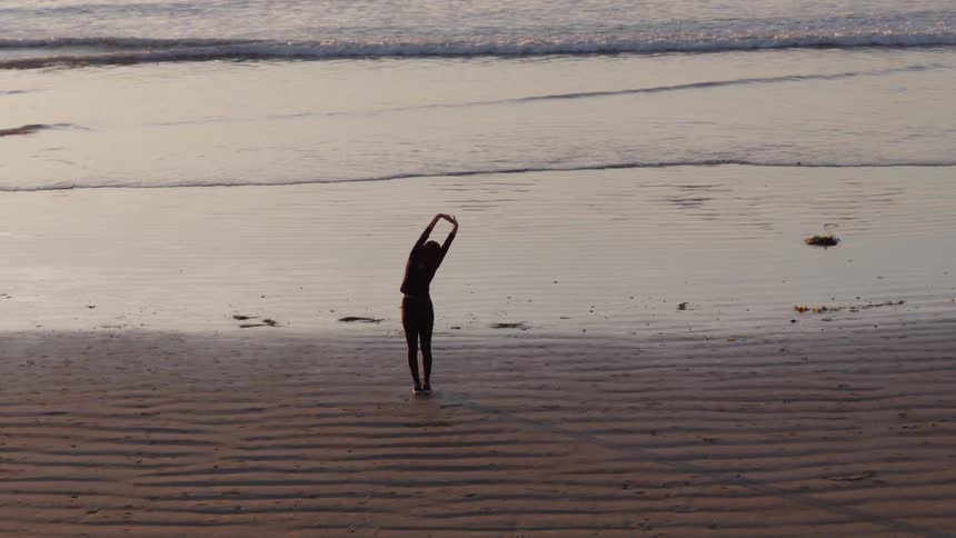 A woman stretches on a beach at sunset