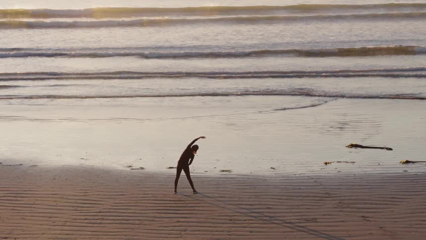 A person stretches on a beach at sunset