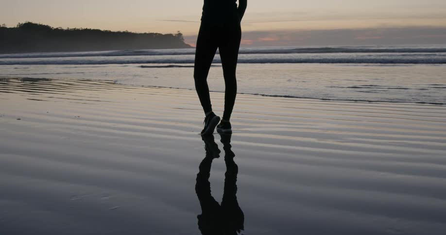 A woman stands on the beach near the water at sunset