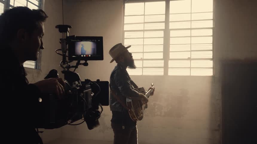 Man filming another man playing guitar in empty building