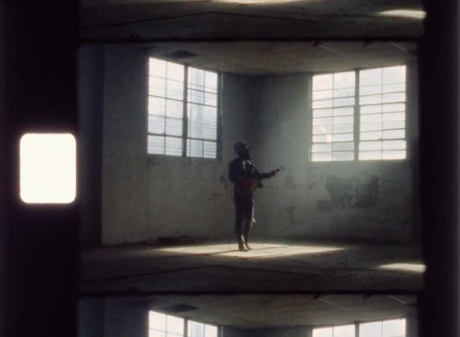 A man stands in an abandoned building playing guitar