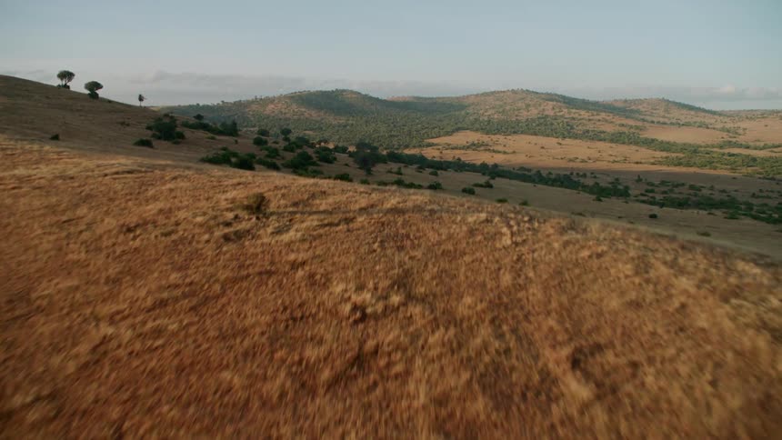Hilly area of brown with some green growth here and there with some clouds in the sky
