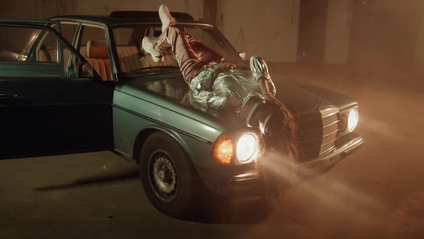 Woman wearing virtual reality headset is laying on hood of car