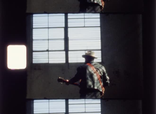 A man is playing a guitar inside an abandoned warehouse in daylight