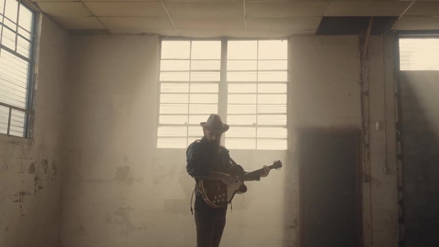 A guitarist stands in an empty room with a guitar