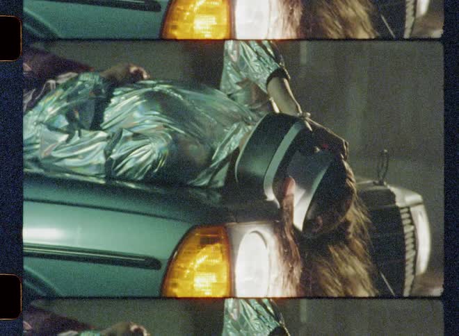 A woman lays on a car hood using a virtual reality headset