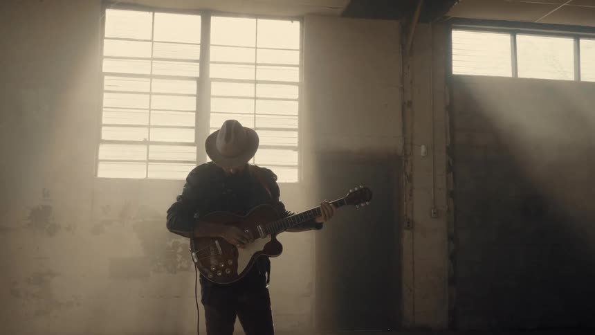 Man wearing hat is playing guitar in empty building