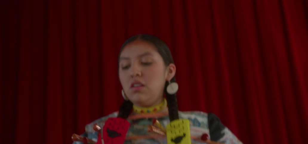 Woman wearing native american dress hops in front of a red curtain
