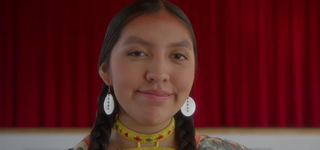 An american indian woman in costume is smiling as she stands in front of a stage
