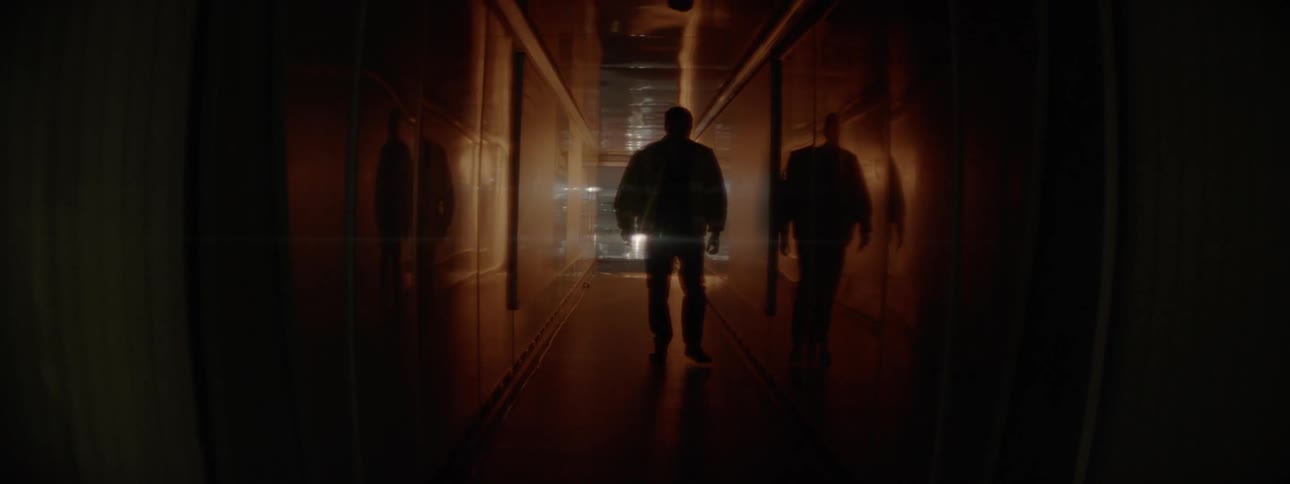 A man is walking down the long dark hall