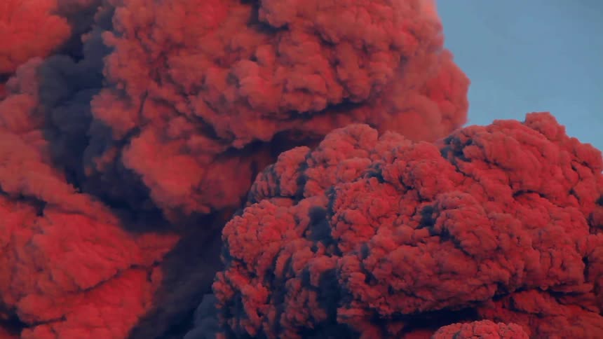 Smoke from a volcano fire is billowing up into the sky in daylight
