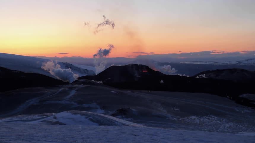 A volcano is giving steam and lava on the hills at sunset