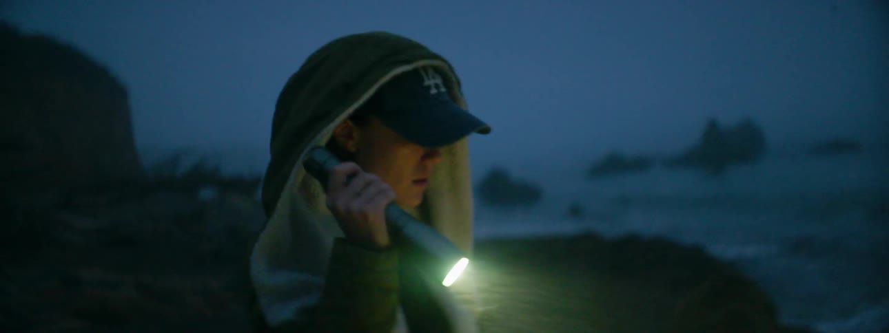 A woman shines a flashlight on the beach at night