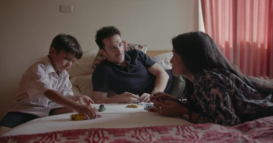 A mother, father and child play on a bed