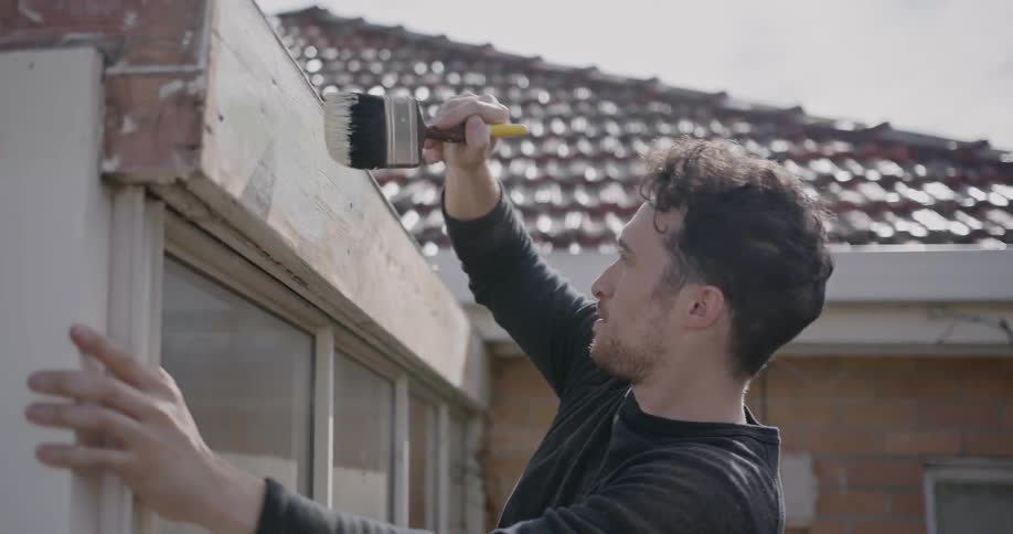 A man applies paint to the facade of a house