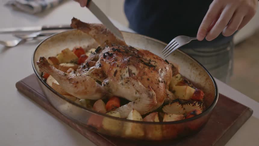 A man is cutting up a cooked chicken