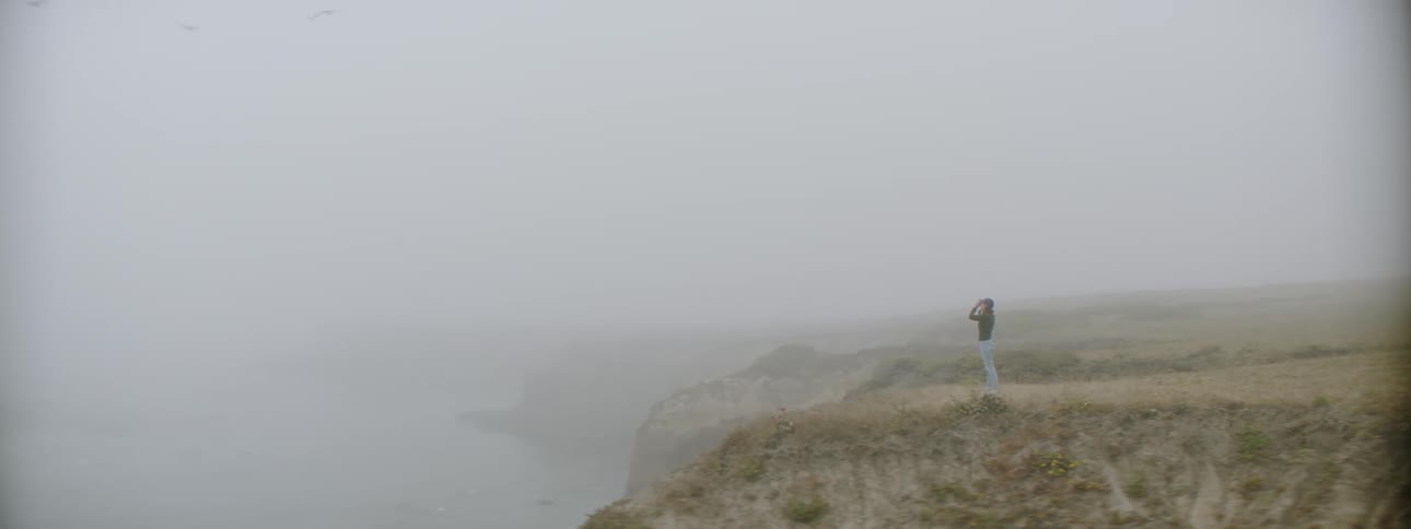 A person is taking photographs near the foggy shore