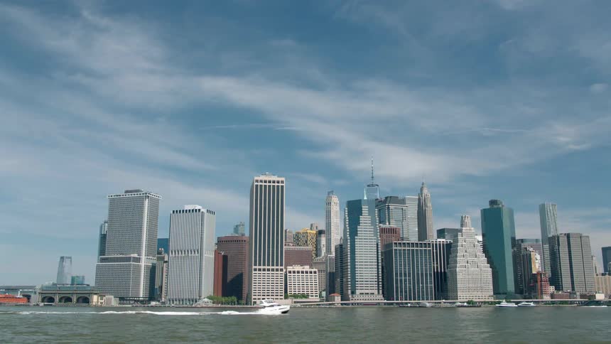 A boat travels on the water in front of tall city buildings
