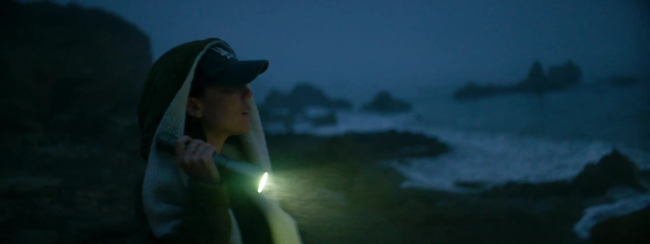 A woman shines a flashlight while walking on the beach at night