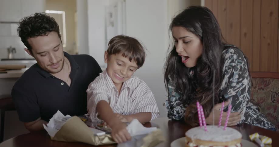 A boy unwraps his birthday present while sitting on his dad's lap