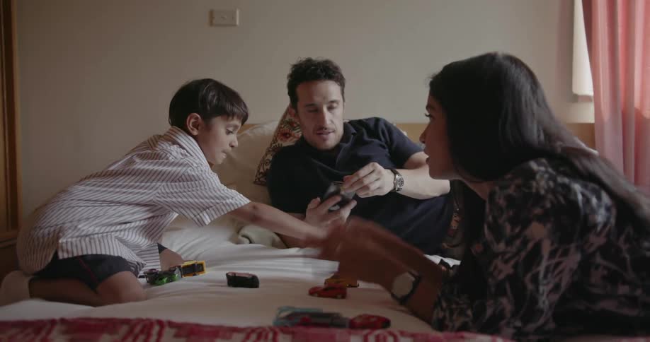 Man woman and child sit on a bed playing with toy trucks