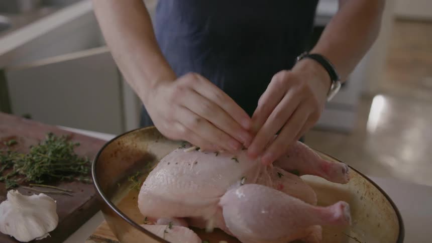 A man is dicing up some garlic and putting it on a chicken in a baking dish