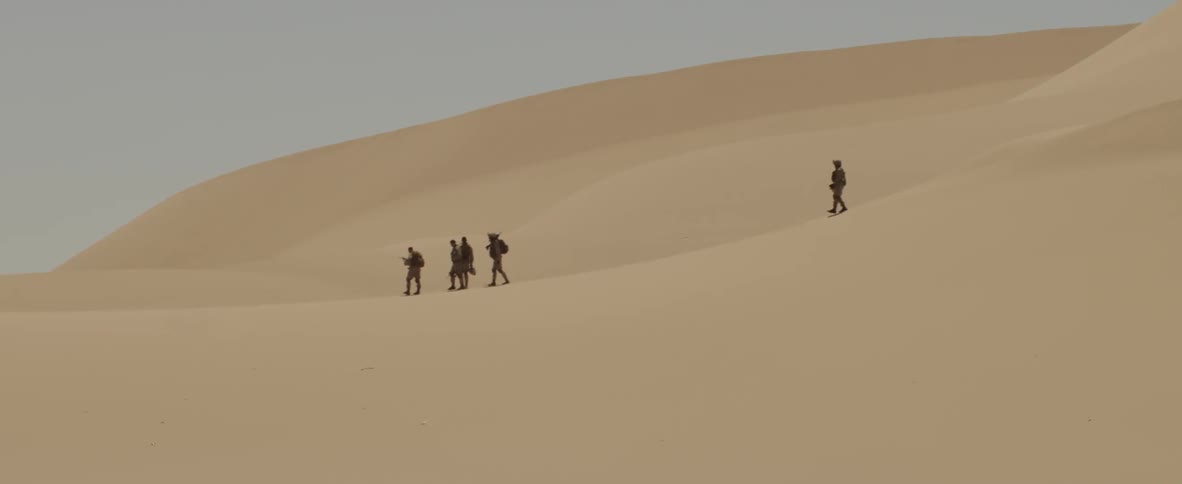 A group of people hike on sand dunes in the desert